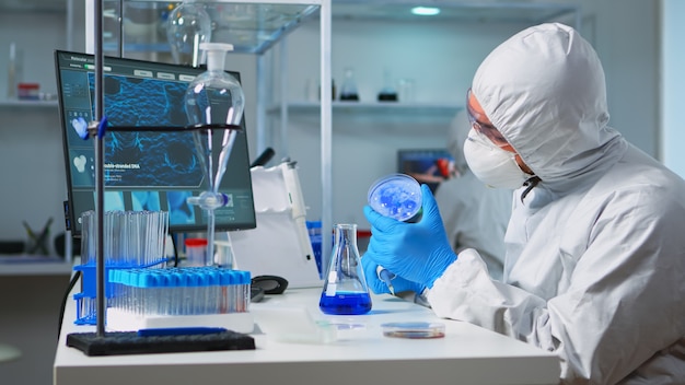 Químico en traje de ppe con micropipeta para llenar tubos de ensayo en un moderno laboratorio equipado. Equipo de científicos que examinan la evolución del virus utilizando alta tecnología para el desarrollo de vacunas contra covid19