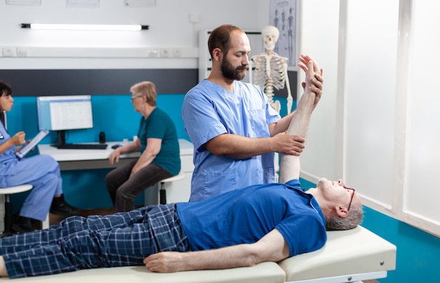 Quiroptractor haciendo masaje osteopático en paciente anciano para la recuperación de los músculos de la mano. Enfermera que brinda asistencia para estirar la articulación del brazo del hombre mayor para el tratamiento de la osteopatía y la atención médica.