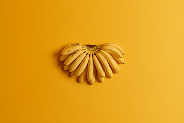 El racimo de pequeños plátanos maduros contienen nutrientes esenciales para la salud aislados sobre fondo amarillo. Concepto de frutas de verano. Vista plana endecha, superior. Fuente natural de vitaminas. Dieta y alimentación sana