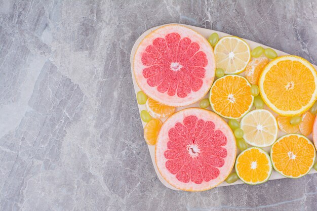 Foto gratuita racimo de rodajas de frutas y uvas sobre tabla de madera.