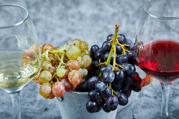 Racimo de uvas blancas y negras y dos copas de vino blanco y tinto sobre azul.