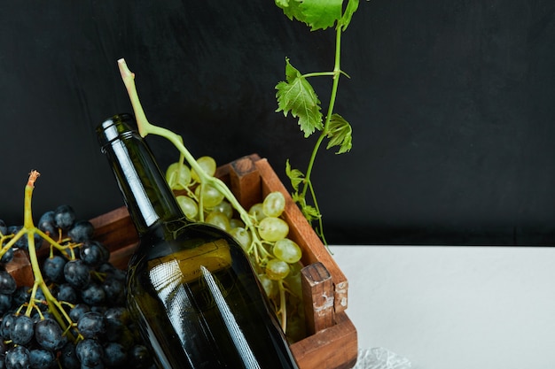 Un racimo de uvas y una botella de vino sobre una mesa blanca. Foto de alta calidad