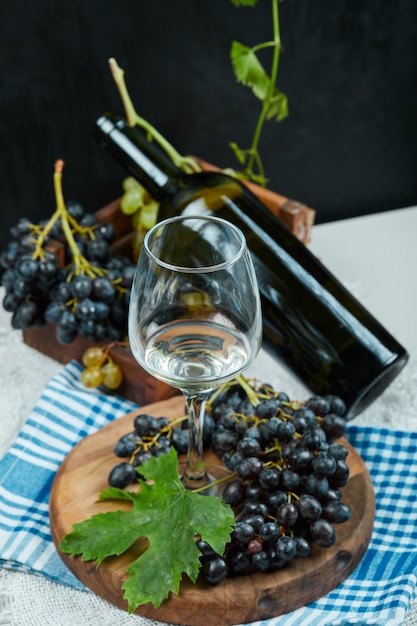 Un racimo de uvas con una copa de vino y una botella de mesa blanca con mantel azul. Foto de alta calidad