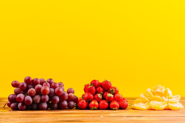 Racimo de uvas; Fresas y rodaja de naranja en mesa de madera sobre fondo amarillo