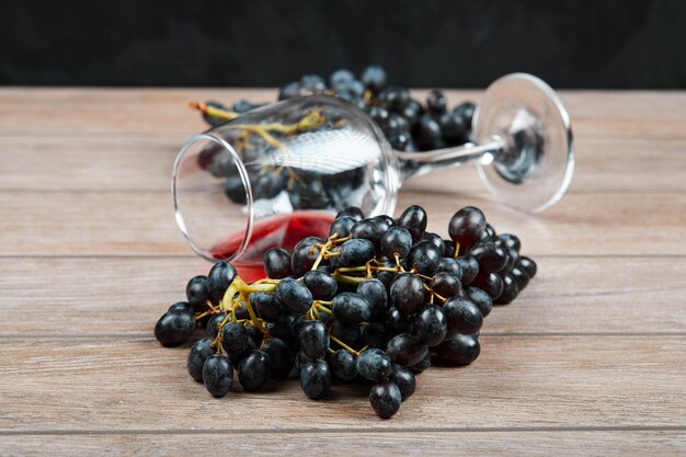 Un racimo de uvas negras y una copa de vino sobre fondo de madera. Foto de alta calidad