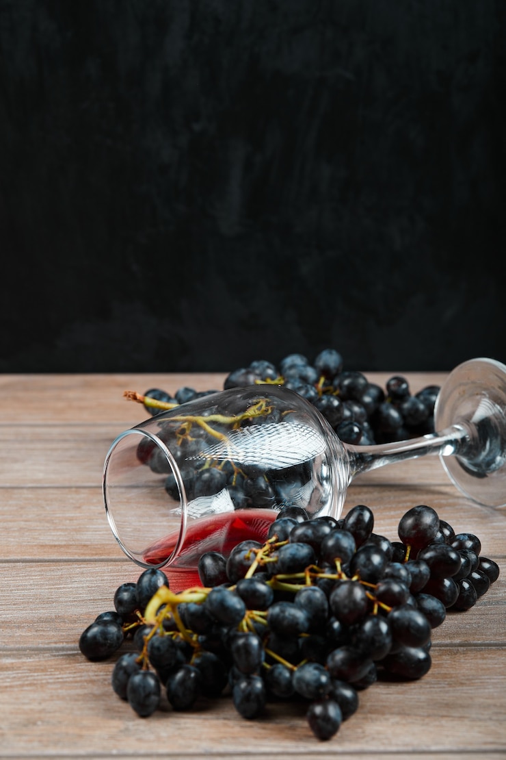 Foto gratuito un racimo de uvas negras y una copa de vino sobre fondo oscuro. foto de alta calidad