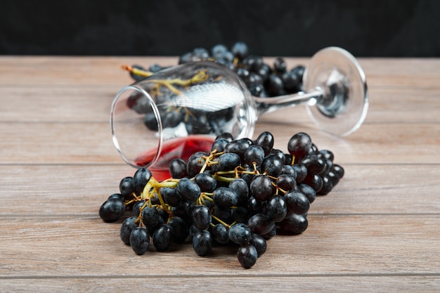 Foto gratuita un racimo de uvas negras y una copa de vino sobre la superficie de madera