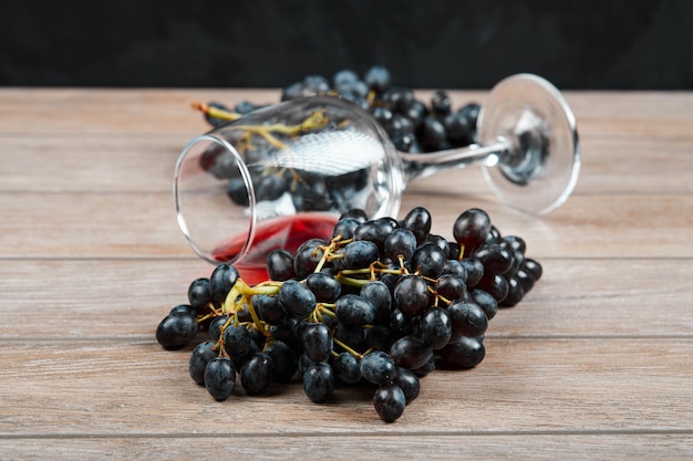 Un racimo de uvas negras y una copa de vino sobre la superficie de madera