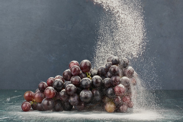 Foto gratuito racimo de uvas negras decoradas con polvo sobre mesa de mármol