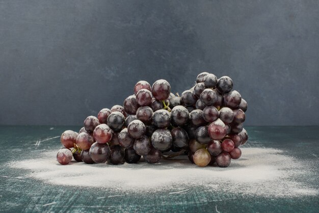 Racimo de uvas negras decorado con polvo sobre mesa de mármol.