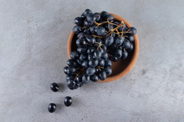 Racimo de uvas negras frescas colocadas en cuenco de barro.