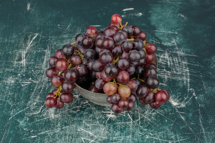 Foto gratuito un racimo de uvas negras en el jarrón de mesa de mármol.