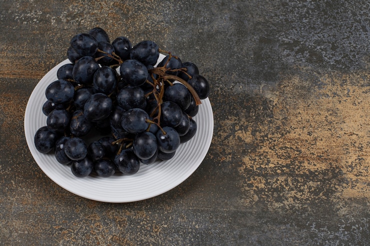 Foto gratuito racimo de uvas negras en plato blanco.