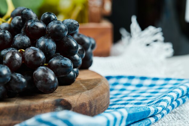 Un racimo de uvas negras sobre placa de madera con mantel azul. Foto de alta calidad