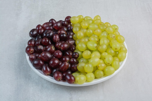 Foto gratuita racimo de uvas púrpuras y verdes en plato blanco. foto de alta calidad