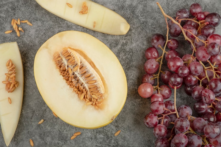 Foto gratuito racimo de uvas rojas maduras y melón en rodajas sobre superficie de mármol.