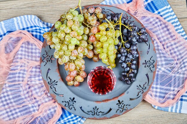 Racimo de uvas y un vaso de jugo en plato de cerámica con manteles.