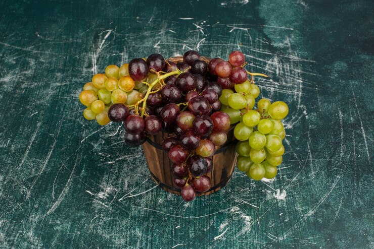 Foto gratuito un racimo de uvas verdes y negras sobre la mesa de mármol.