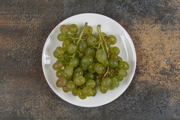 Racimo de uvas verdes en plato blanco.