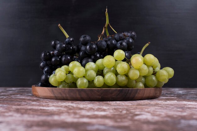 Un racimo de uvas verdes y rojas en una bandeja de madera sobre negro