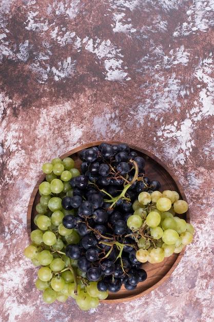 Un racimo de uvas verdes y rojas en una bandeja de madera