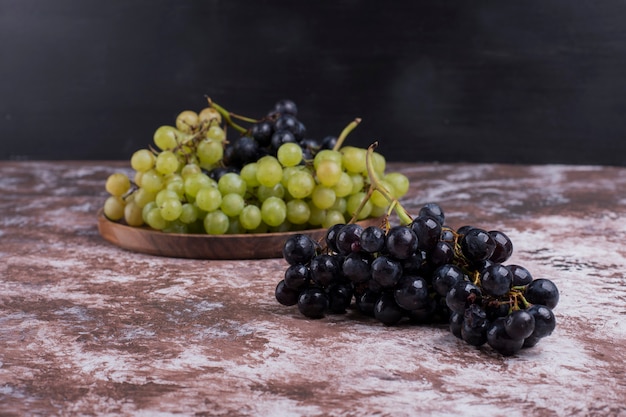 Un racimo de uvas verdes y rojas en una bandeja de madera