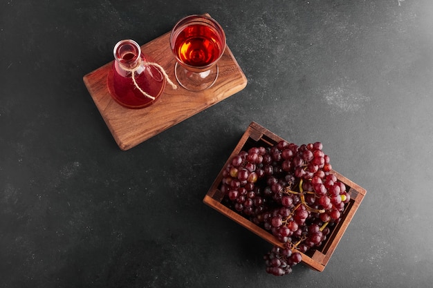 Racimos de uva roja en una bandeja de madera con una copa de vino, vista superior.