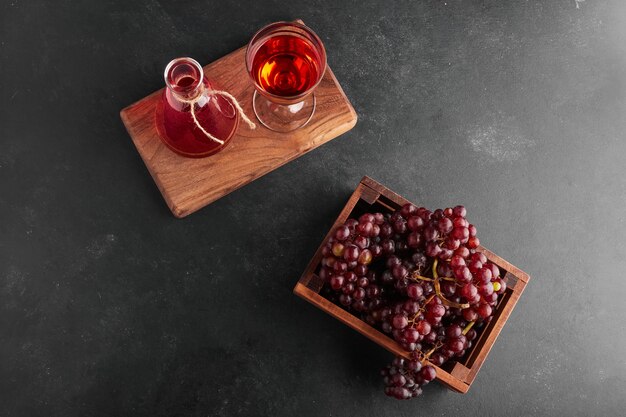 Racimos de uva roja en una bandeja de madera con una copa de vino, vista superior.