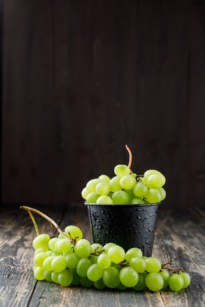 Racimos de uvas en un mini cubo en la superficie de madera, vista lateral.