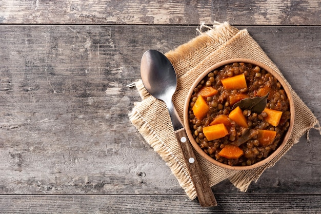 Ragout de estofado de lentejas con calabaza y zanahoria en un tazón sobre mesa de madera