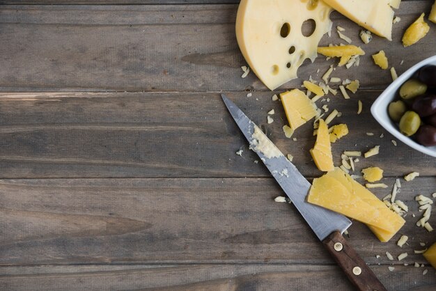 Rallado y rebanadas de queso maasdam y cheddar en mesa de madera con cuchillo