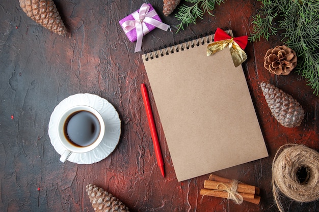 Ramas de abeto accesorios de decoración conos de coníferas regalo y cuaderno una taza de té negro sobre fondo oscuro