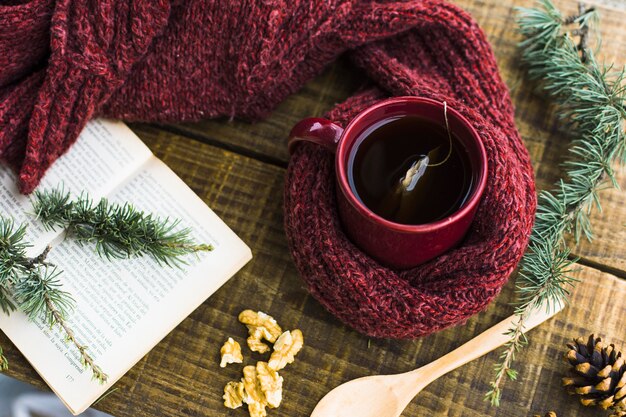 Ramas de coníferas y libro cerca de té y suéter