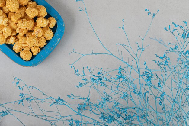 Ramas decorativas junto a una pequeña fuente de palomitas de caramelo sobre fondo de mármol.