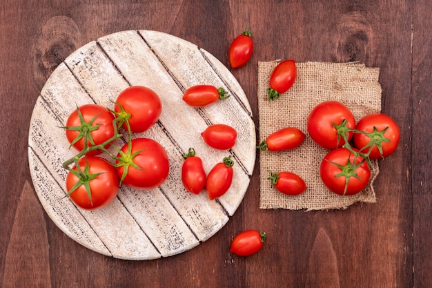 Ramas de tomates cherry sobre tabla de madera cerca de los tomates en cilicio sobre madera