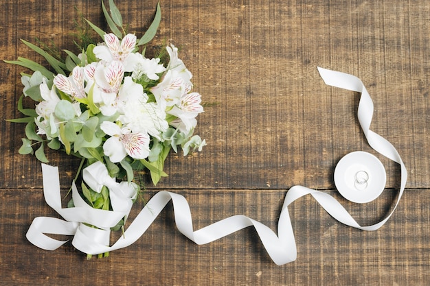 Ramo blanco de la cinta y de la flor con los anillos de bodas en la placa sobre el escritorio de madera