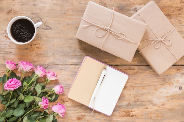 Ramo de flores con cajas de regalo; Diario y té negro sobre fondo de madera.