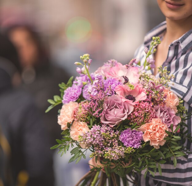 Ramo de flores en colores pastel y claros abrazados por una dama en la calle