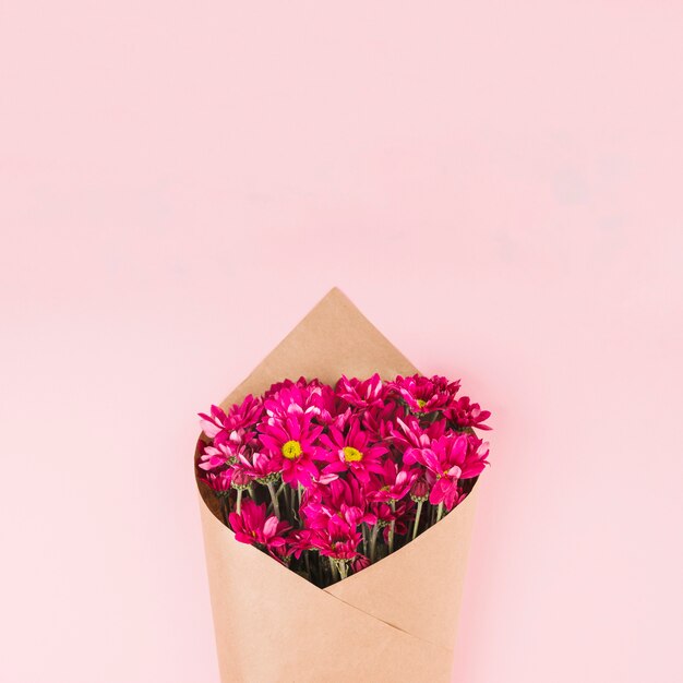 Ramo de flores envuelto con papel marrón sobre fondo rosa