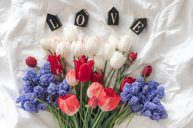 Un ramo de flores frescas y una palabra decorativa amor en una vista superior de la cama blanca