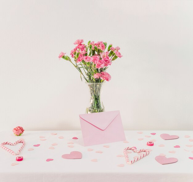 Ramo de flores en jarrón cerca de un conjunto de corazones de papel, sobre y bastones de caramelo