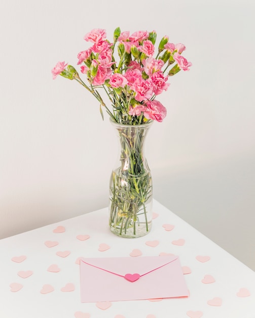 Ramo de flores en jarrón cerca de corazones de papel y sobre en mesa