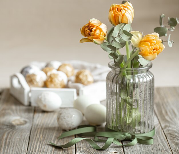 Un ramo de flores en un jarrón de cristal con elementos decorativos sobre un fondo difuminado. Concepto de vacaciones de semana Santa.