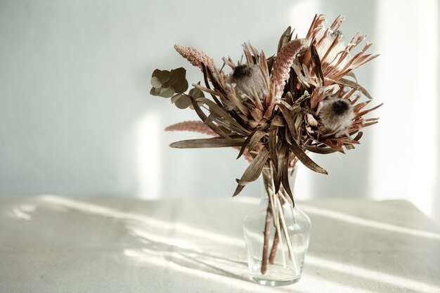 Un ramo de flores secas en un jarrón de vidrio sobre un fondo claro con luz solar.