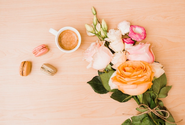 Ramo de flores con taza de café y macarrones en escritorio de madera