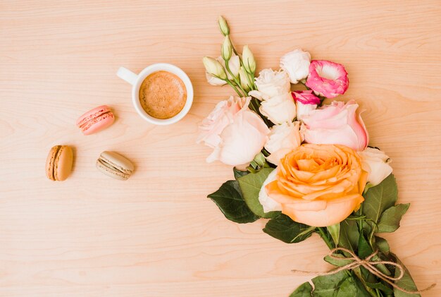 Ramo de flores con taza de café y macarrones en escritorio de madera