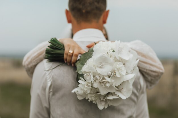 Ramo de novia blanco hecho de callas y una mujer abraza a un hombre al aire libre