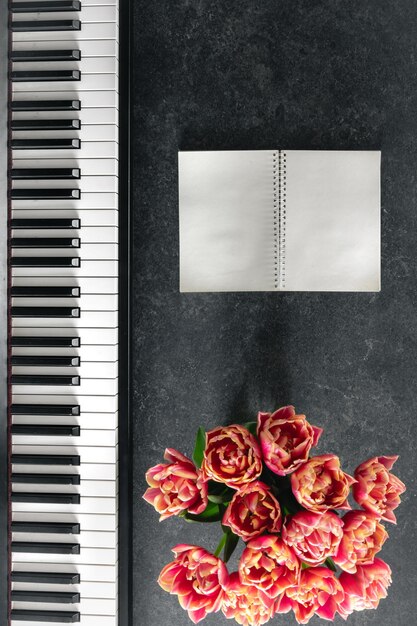 Ramo de piano de flores de tulipán y bloc de notas en un fondo oscuro vista superior