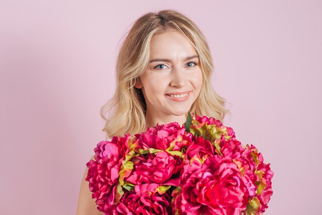 Ramo rojo de las rosas de la flor delante de la mujer joven sonriente contra el contexto rosado