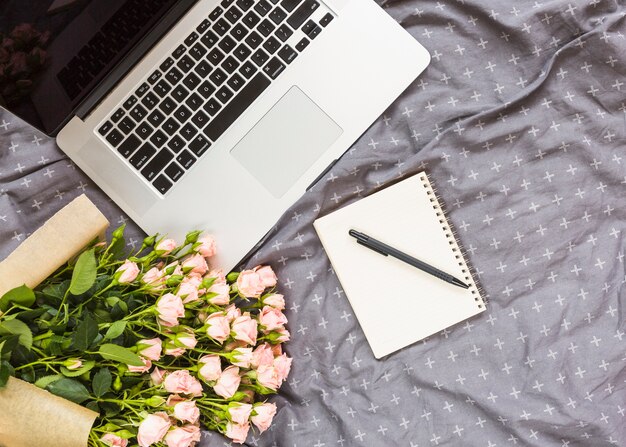 Ramo de rosas; bolígrafo; Bloc de notas de espiral y laptop en textil gris.